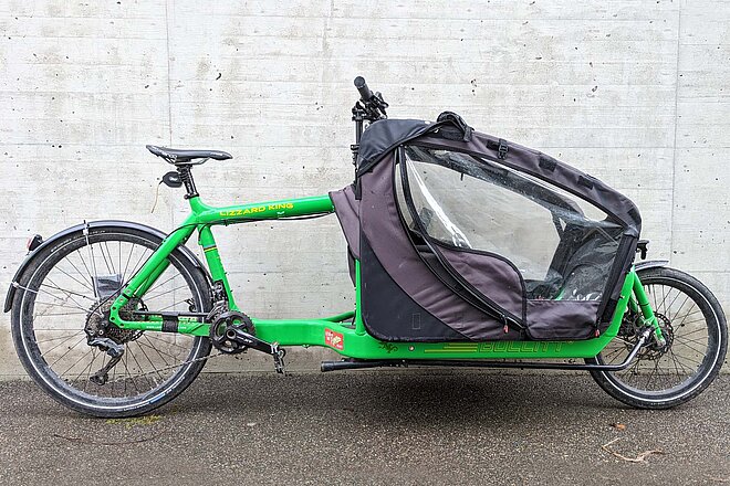 Das «Bullitt» ist robust und langlebig, für das «Canopy» gilt das aber nicht. Bullitt Cargobike Test. Ein grünes Lastenrad steht vor einer Betonwand.